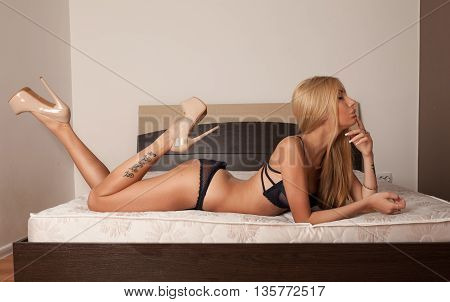 Slim sexy beautiful blond woman in black lingerie laying on bed. Beauty blonde woman with attractive buttocks in lace lingerie. Female ass in underwear