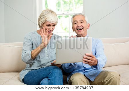 Happy senior couple looking into digital tablet while sitting on sofa at home