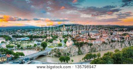 Evening View Of Tbilisi At Colorful Sunset, Georgia. Summer Cityscape. On Photograph Visible A New Concert Hall, Avlabar Residence - Presidential Administration Of Georgia, Holy Trinity Cathedral Of Tbilisi, Metekhi Church, Old Historic District Abanotuba
