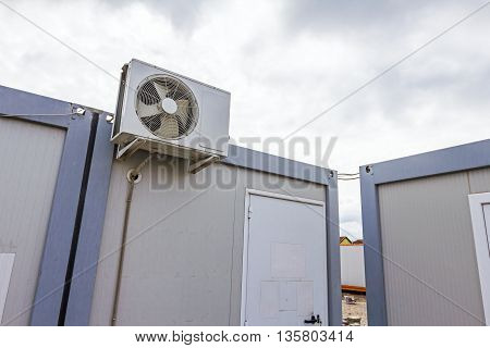 Outdoor unit compressor of air conditioner is placed on white container office.