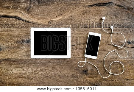 Phone with headphones and tablet pc on wooden background. Mockup screen electronic devices. Flat lay