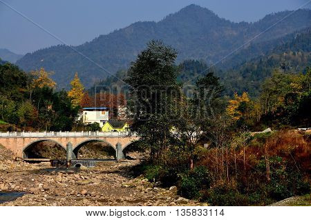 Bai Lu China - November 17 2013: A rocky river bed spanned by an arched bridge with distant mountains