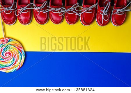 A lot of small red boat shoes near big multi-colored lollipop on colored background. Top view copy space. Frame. group of child boat shoes.