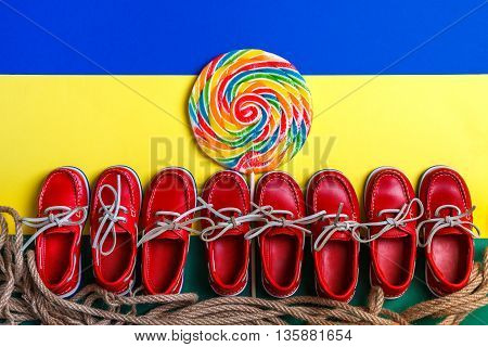 A lot of small red boat shoes near big multi-colored lollipop on colored background. Top view copy space. Frame. group of child boat shoes.