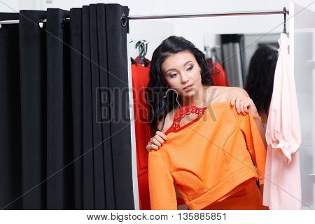 Can you bring me on more dress please. Fashionable young woman shopping in a clothing store. Woman shopper in a fitting room. Woman shopping for dress. Woman shopaholic. Fashion shopping