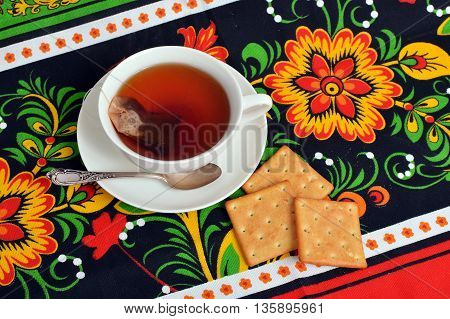 Cup with tea and biscuits on colorful tablecloth