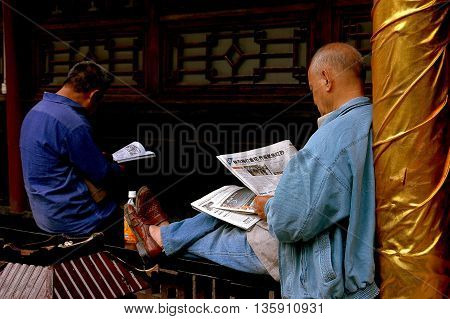 Chengdu China - September 20 2006: Two men reading Chinese newspapers sitting on a wooden gallery balustrade at the Da Ci Buddhist Temple