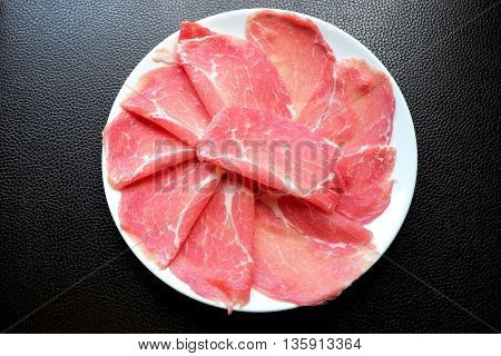Fresh sliced pork on white dish with black leather background for Japanese hot pot.