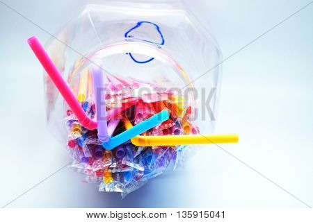 Colorful plastic drinking straws in plastic wraps with transparent bowl on blue-white background. Focus on extended straws. Space for texts.