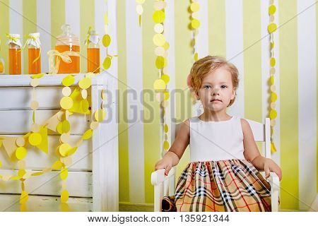 Beautiful little girl.Blue-eyed blonde.White chair.Lemonade.Children's room. Happy small girl portrait.