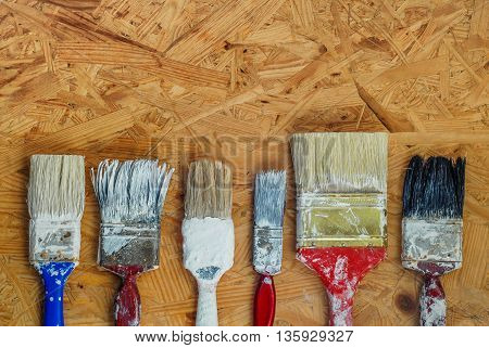 Old paint brushes on pressed wooden panel background