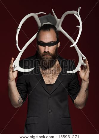 Brutal bearded man with horns. On red background. Man in black suit. fashion studio shot.