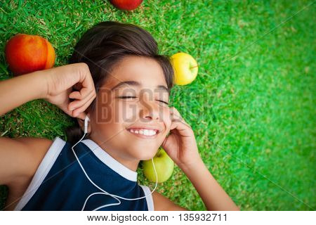 Portrait of a cute smiling teen boy listening to music, lying down on a fresh green grass field, happy summer weekend, spending time outdoors