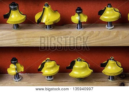 wooden shelf of assorted yellow metal router bits on red background