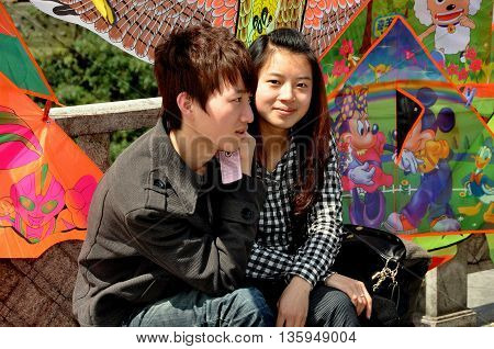 Dujiangyan China - April 8 2011: Romantic young Chinese couple sitting next to a display of colourful kites in a Min River park