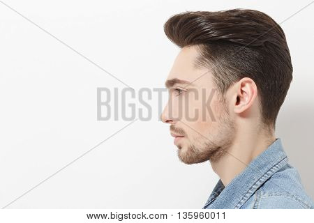 Profile of handsome young man injeans shirt posing over white background. Male with modern hairstyle in studio. Hairdressing concept.