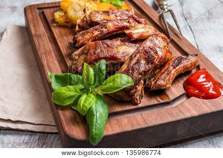 elicious Grilled Pork Rib and Fried Potato Wedges with Sauce on wooden cutting board, white wooden background