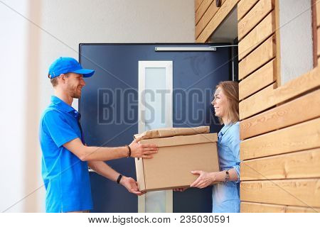 Smiling delivery man in blue uniform delivering parcel box to recipient - courier service concept. Smiling delivery man in blue uniform