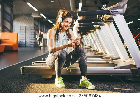 Beautiful Young Caucasian Girl Sportswoman Sitting, Resting After Training On Treadmill Against The 