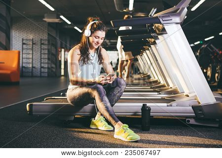 Beautiful Young Caucasian Girl Sportswoman Sitting, Resting After Training On Treadmill Against The 