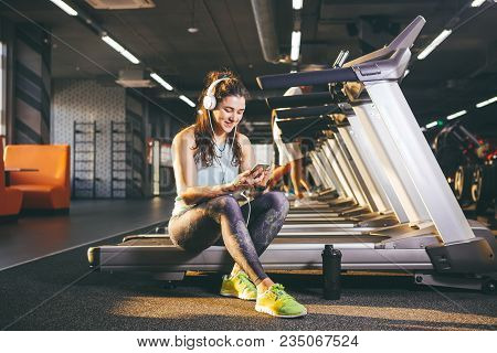 Beautiful Young Caucasian Girl Sportswoman Sitting, Resting After Training On Treadmill Against The 