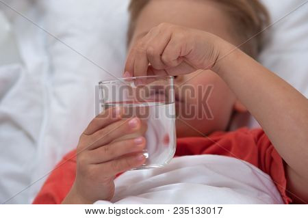 Little Sick Cute Cboy Holding A Pill And A Glass Of Water Lying On The Bed