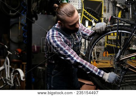 A Handsome Stylish Male Wearing A Flannel Shirt And Jeans Coverall, Working With A Bicycle Wheel In 