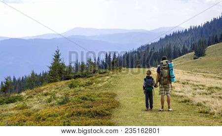Father And Son With Backpacks Hiking Together In Scenic Summer Green Mountains. Dad And Child Standi