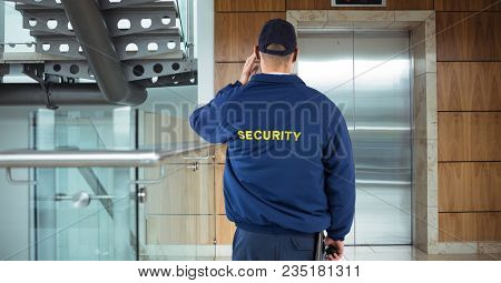 Rear view of security guard waiting for lift while standing in office building