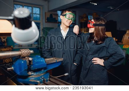 Group Of Working Young Woman And Male Turner Engineers Are Standing Behind An Automatic Lathe. Conce