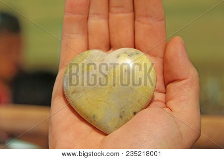 The Hand Holds A Heart Made Of Natural Stone Yellow Jadeite. Heart In Hand. A Stone In The Shape Of 