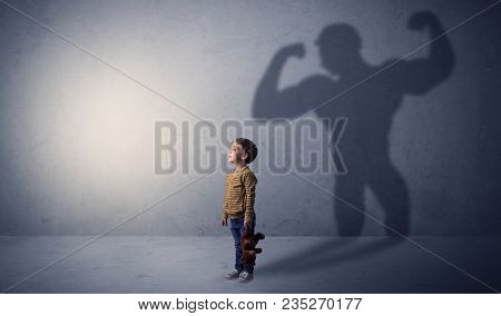 Little waggish boy in an empty room with musclemen shadow behind