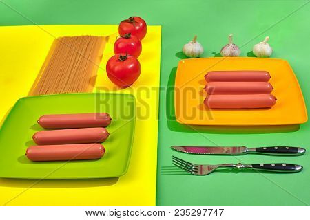 A Lot Of Raw Sausages On Plate. On Green And Yellow Background With Pasta And Vegetables, Top View. 