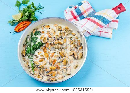 Mussels In Milk Cream Y Sauce With Aromatic Herbs And Lemon In Red Cooking Pan. Blue Background.