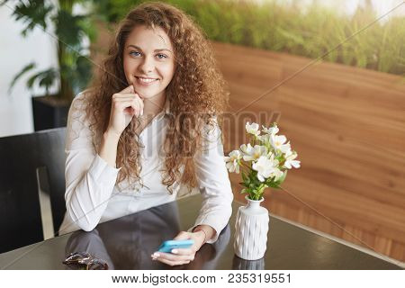 Happy Beautiful Satisfied Young Woman With Broad Smile, Holds Cell Phone, Surfes Social Networks Or 