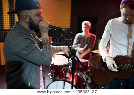 Band Of Young Musicians Performing In Dim Recording Studio Making New Album, Singer With Mic In Fore