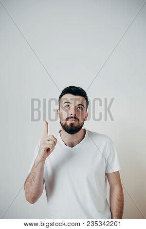 Vertical Picture Of A Guy That Stands At The Wall. He Is Pointing Up And Looks Up As Well. Man Has A
