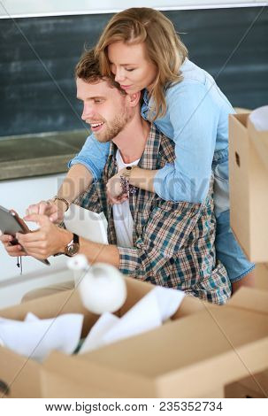 Young couple moving in new home.Sitting and relaxing after unpacking.Looking something on laptop. Young couple