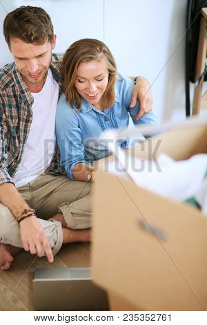 Young couple moving in new home.Sitting and relaxing after unpacking.Looking something on laptop. Young couple