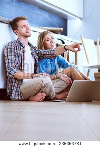 Young couple moving in new home.Sitting and relaxing after unpacking.Looking something on laptop. Young couple