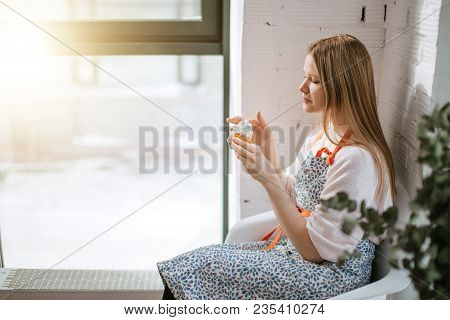 Young Woman Enjoys Her Cupcake While Sitting Near Window With Sunny Flare