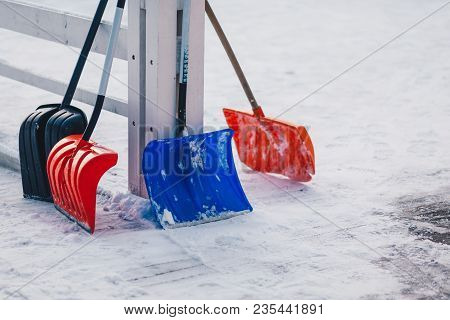 Colourful Four Plastic Shovels Stand On Snow. Winter Time. Shoveling Deep Snow. Season And Cleaning 