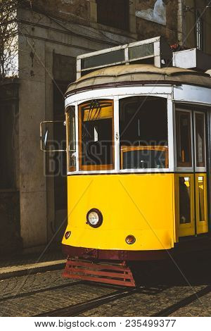 Quaint Yellow Tram On The Rails Of Old And Beautiful Street Of Alfama District Of Lisbon. City Touri