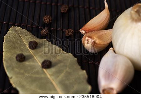 Onion, Garlic, Black Pepper And Bay Leaf On A Black Table