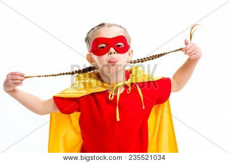 Little Supergirl In Yellow Cape And Red Mask For Eyes Showing Tongue And Holding Pigtails Isolated O