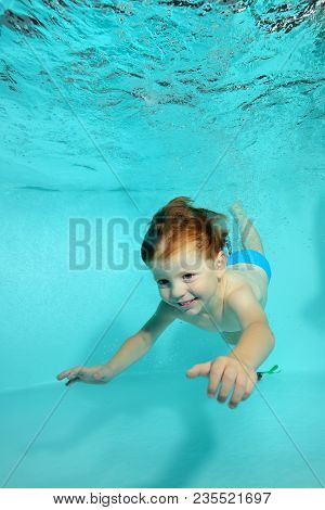 Happy Little Boy Dives Underwater To The Bottom Of The Pool On A Blue Background And Smiles. Portrai