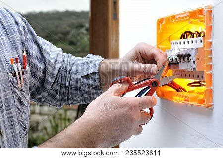 Electrician Technician At Work On A Residential Electric Panel, Cuts The Wire With Scissors