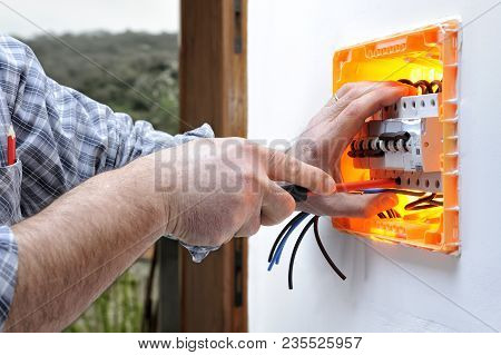 Electrician Technician At Work On A Residential Electric Panel, He Fixes The Wire With The Screwdriv