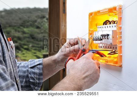 Electrician Technician At Work On A Residential Electric Panel, Cuts The Wire With Scissors