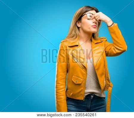 Beautiful young woman with sleepy expression, being overworked and tired, rubbes nose because of weariness, blue background